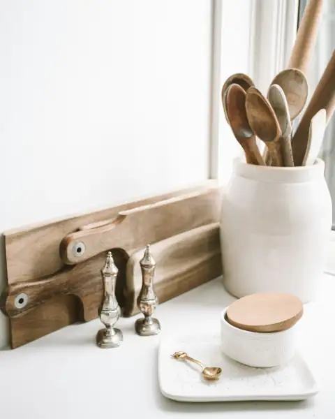 Kitchen tools: brown wooden spoons on ceramic canister on white top surface