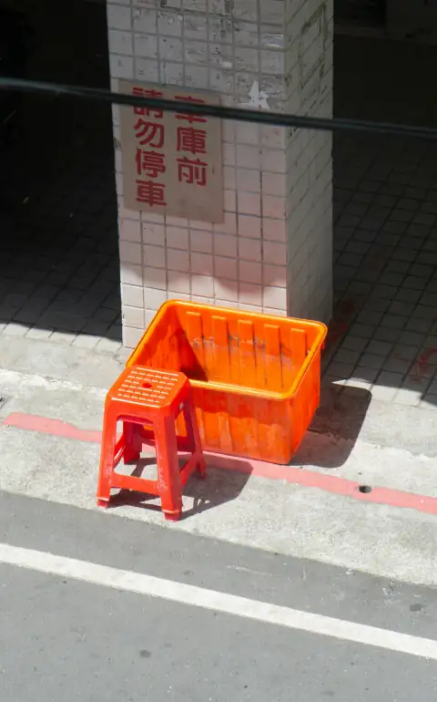 Stools & chairs: An orange plastic crate and a matching stool on a sidewalk by a pillar