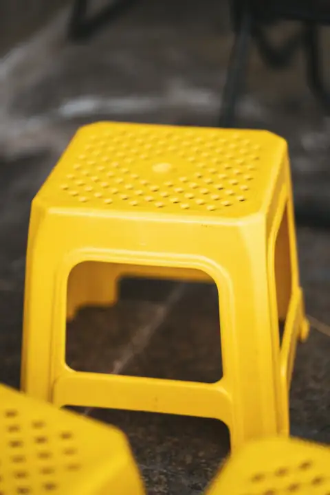 Stools & chairs: A bright yellow plastic stool on a dark surface