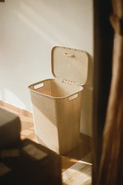 Baskets: a white trash can sitting next to a white wall