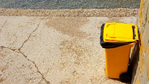 Dustbins: a yellow trash can sitting next to a brick wall